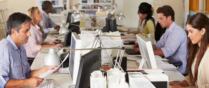 How To Welcome Employees Back Into the Workplace Workers collaborate in small teams in a busy office space