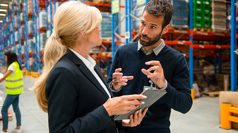 A male and female manager discuss people analytics on computer tablet in warehouse space