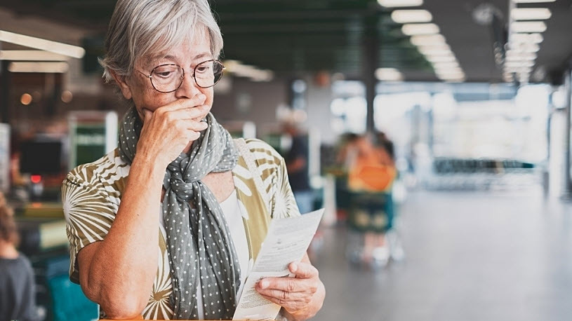 Senior woman frowns looking at grocery store receipt