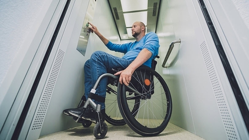 Man who uses a wheelchair pushes button in wheelchair lift elevator