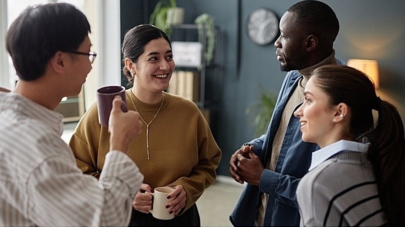 Diverse young employees chatting over coffee in office Diverse young employees chatting over coffee in office
