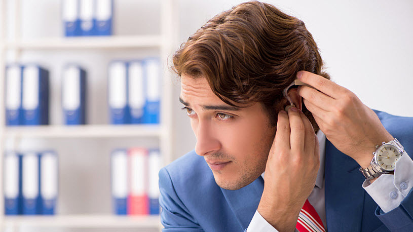 Young white man adjusting hearing ad while working at desk Young white man adjusting hearing ad while working at desk