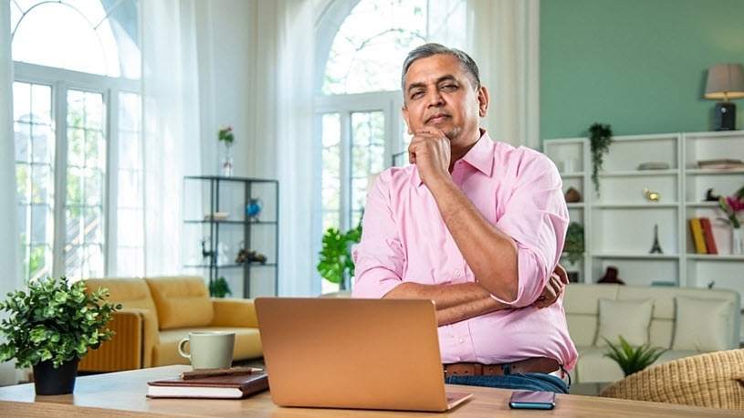 Middle aged man thinks about investments using laptop Middle aged man thinks about investments using laptop