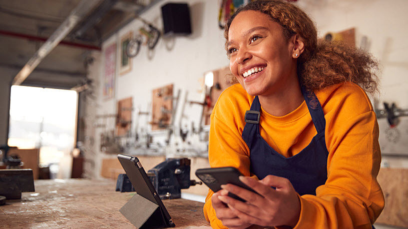 Smiling business owner leaning on shop counter with mobile phone How Small Business Retirement Plans Help Pay for Themselves in Tax Savings