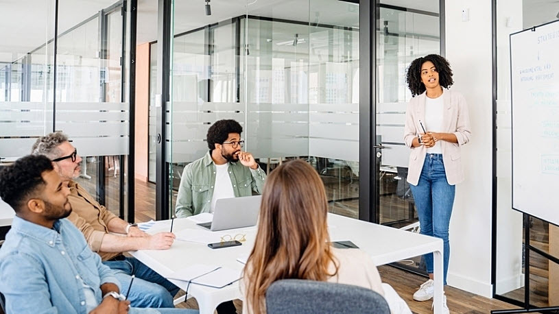 A professional woman stands presenting staffing options to team Moving to Managed Services? Considerations for Staffing Your "Payroll Retained Team"