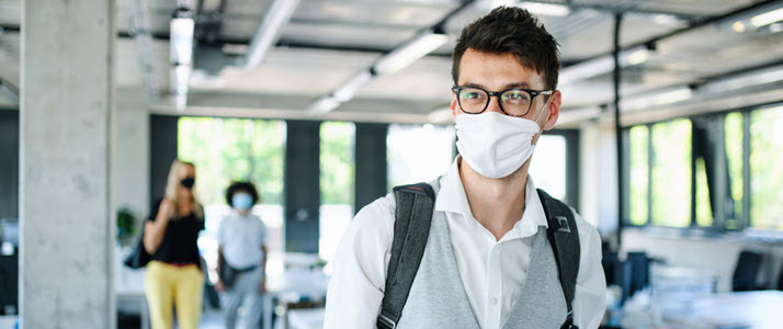 Young man with face mask walking into office Young man with face mask walking into office